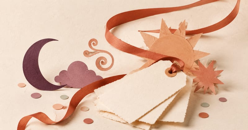 Blank handmade name tags surrounded by a paper moon, storm cloud, sun and swirling ribbon