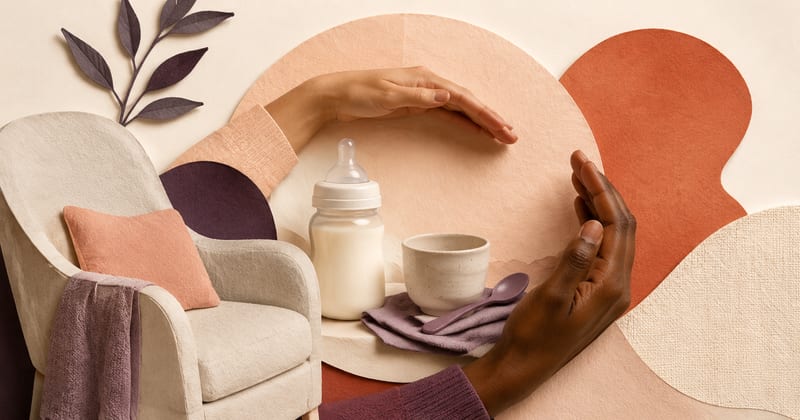 Two hands curved into a protective circle around a bottle of milk and a small cup, beside a nursing chair
