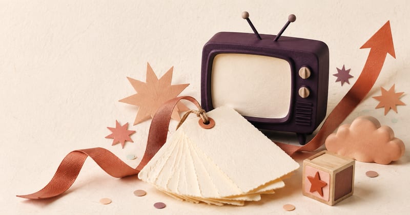 A retro television beside a fanned stack of blank name cards, a rising arrow, paper stars and a wooden block