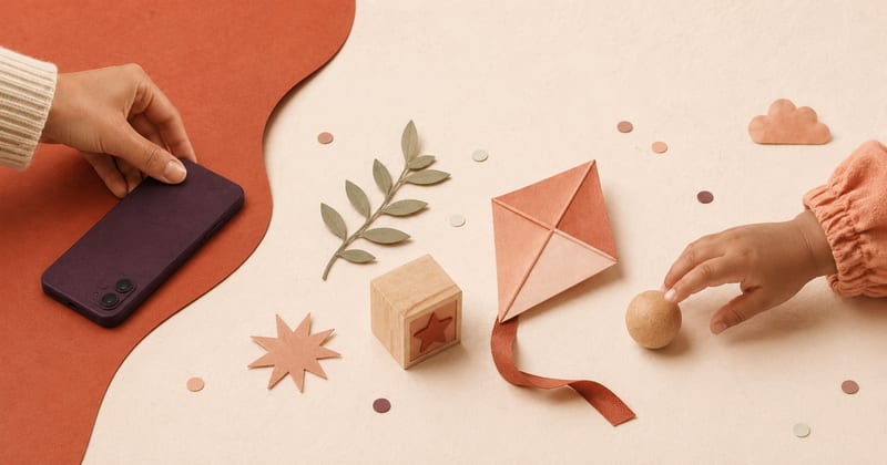 An adult sets a phone aside while a child reaches for a wooden ball, paper kite and block