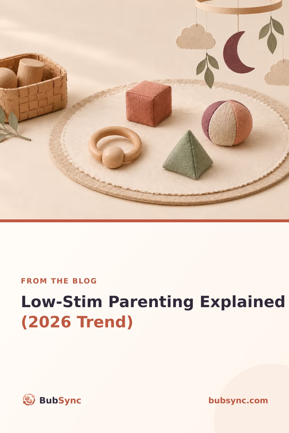 A simple wooden ring rattle and muted fabric shapes arranged on a round felt play mat beneath a sparse paper mobile